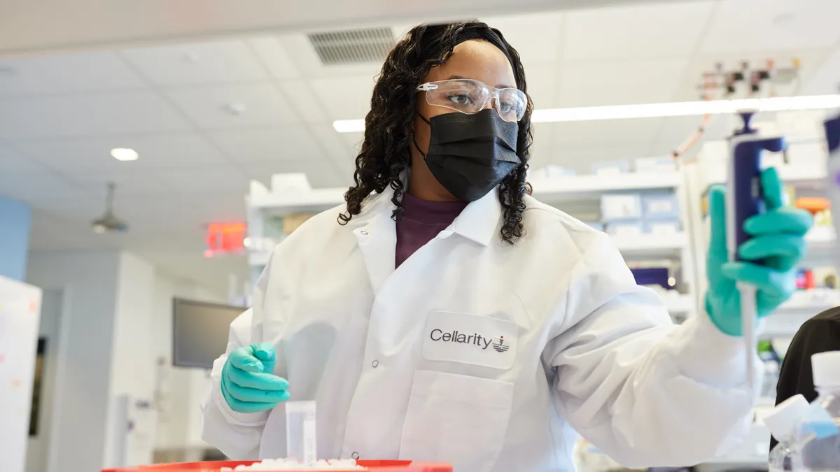 A woman in a lab coat looks at a lab experiment she is performing.