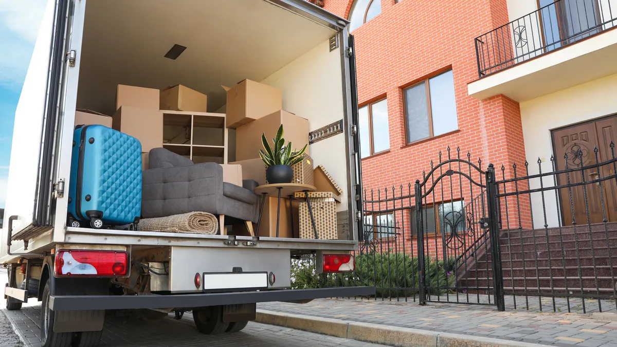 A moving truck stands with its back open on a street next to brick buildings.