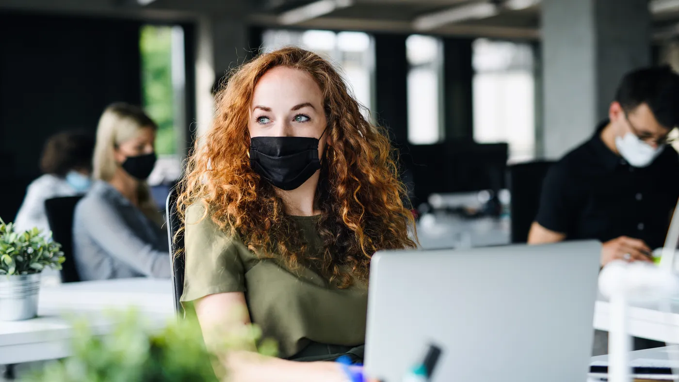 woman using computer in library or office while wearing a facemask