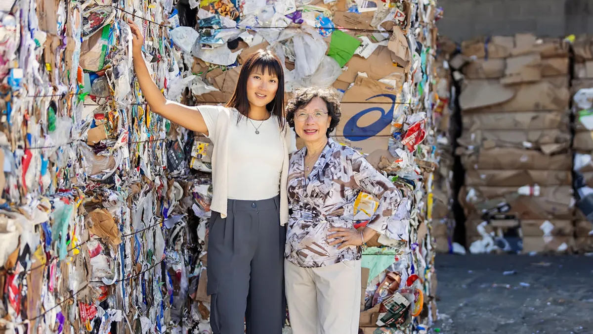 Two women pose near bales of recycled paper