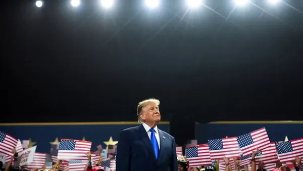 President Donald Trump stands in convention venue with backdrop of people holding American flag posters.