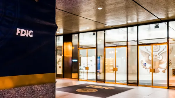 A sign shows the FDIC acronym in the foreground on the left, and glass doors and an FDIC rug in the background to the right.
