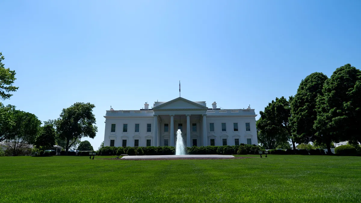 The White House sits in the background on a sunny day. The lawn in front is green.