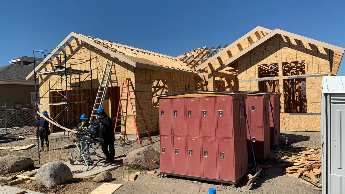 Three construction workers in hard hats stand outside an unfinished single family home.