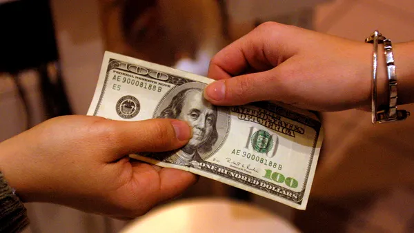 A One-Hundred Dollar Bill being passed from one hand to another