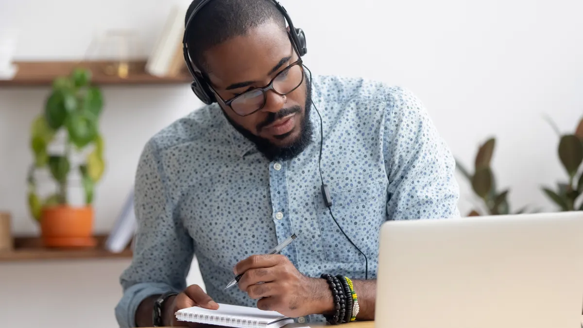 Focused businessman in headphones writing notes watching webinar