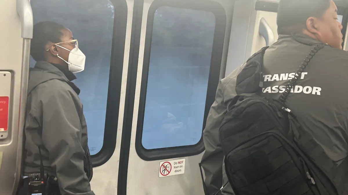 Two people standing inside a train wearing uniforms reading "transit ambassador."