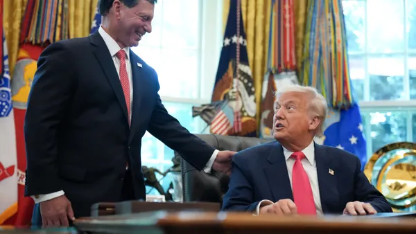 Former Fiserv CEO Frank Bisignano lays hand on shoulder of President Donald Trump in Oval Office with flag in background.