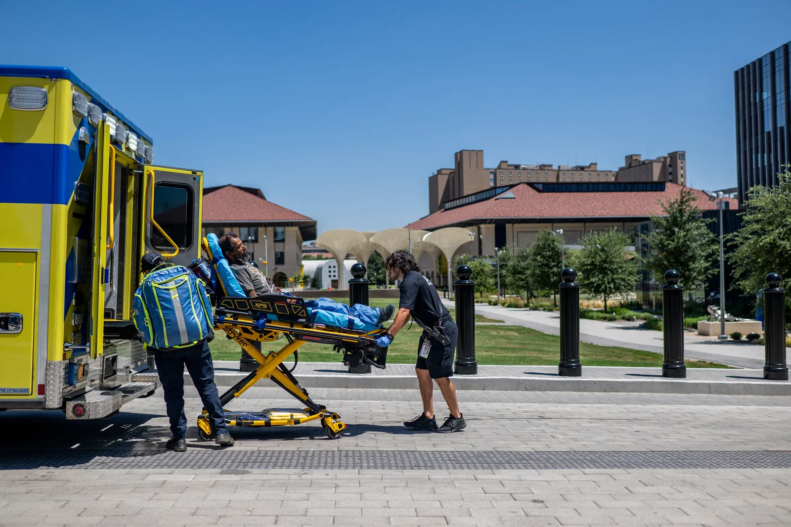 Two people wheel a patient strapped to a gurney onto a vehicle