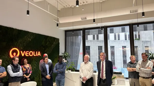 A group of people stand in a Boston office space, with the Veolia logo on a green wall to the left