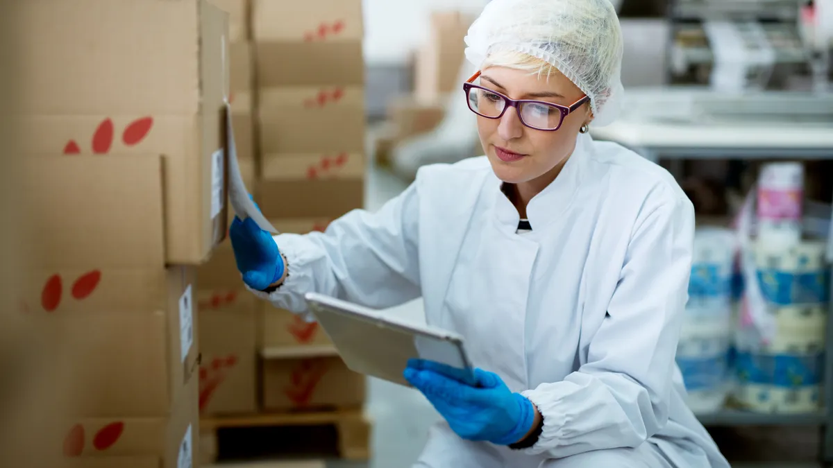 Young beautiful focused female worker in sterile cloths using a tablet to check correction of inventory in factory storage room