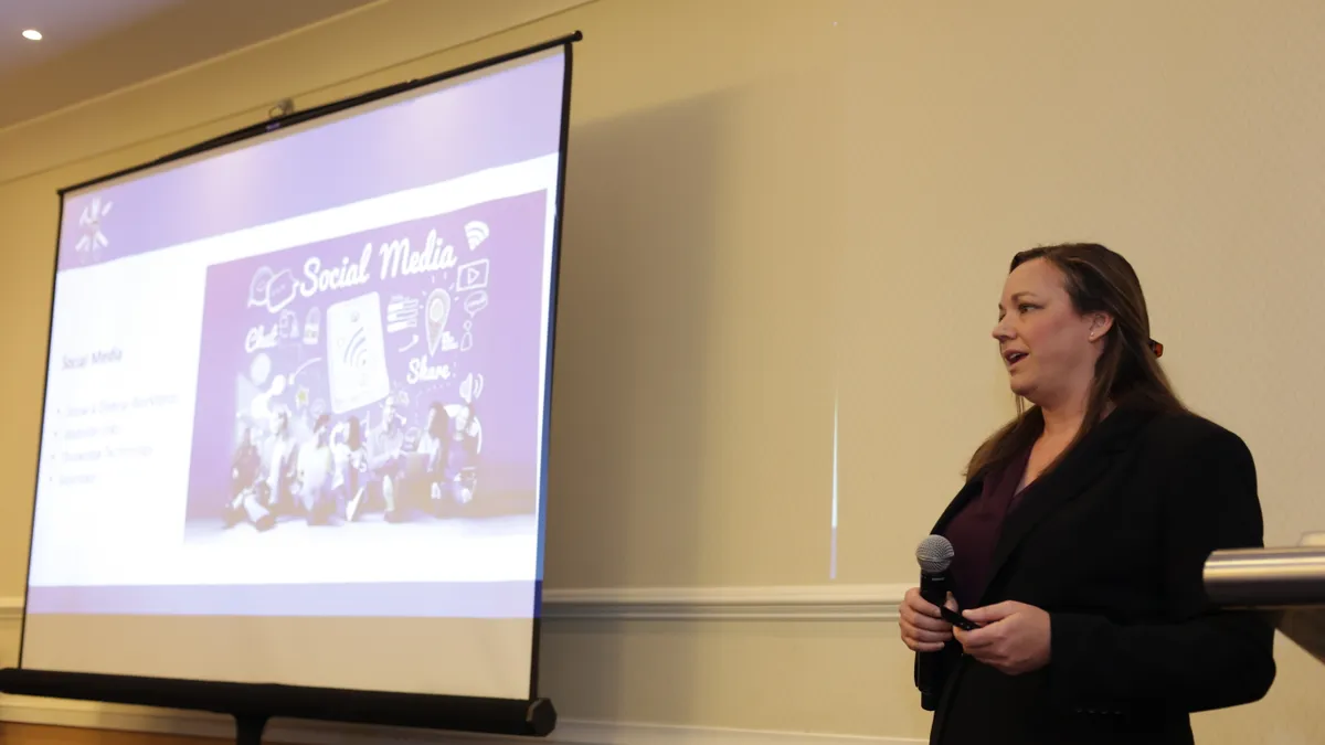 A woman presents in front of a large video screen