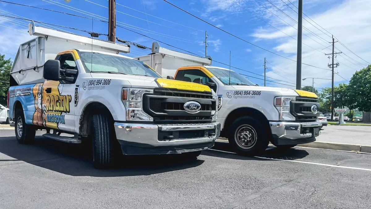 Two pickup trucks, with a raccoon logo, in a parking lot