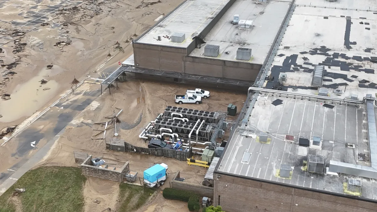 An overhead view of an industrial building affected by flooding, the surrounding exterior is covered in dirt and sediment.