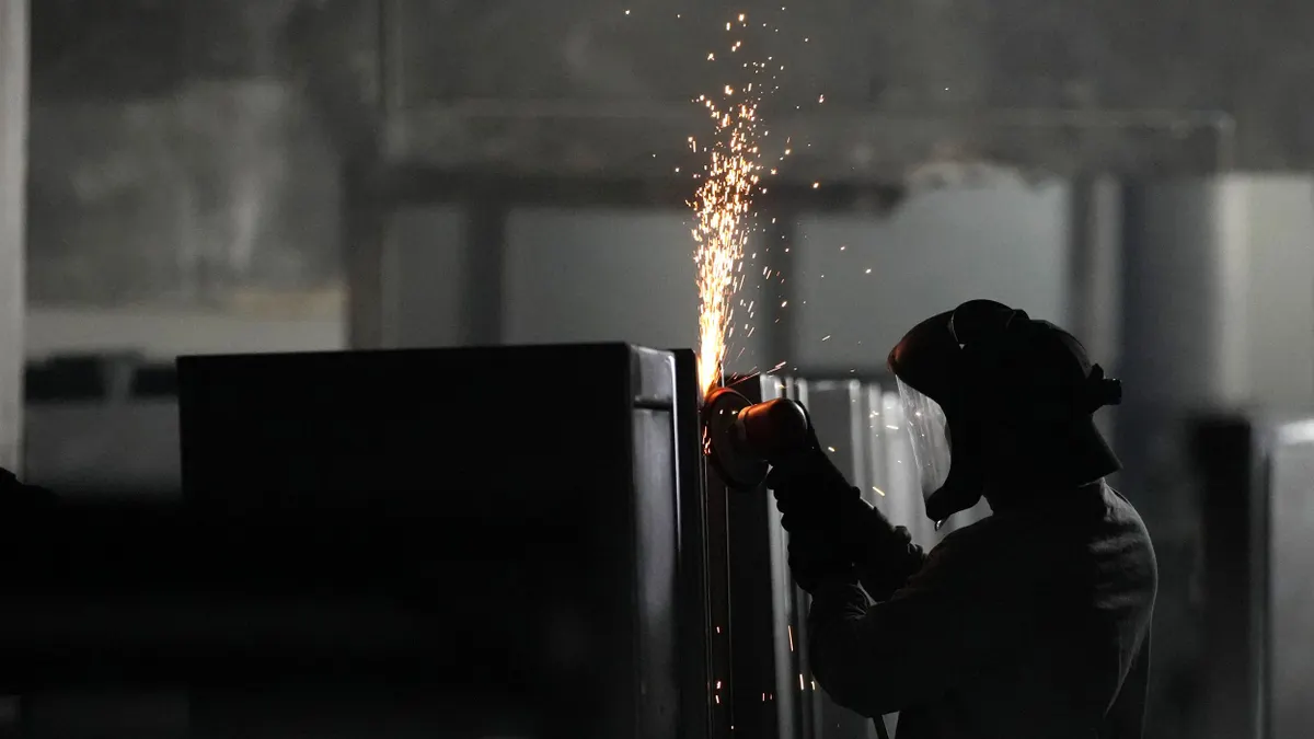 A person wearing a helmet and gloves as they weld a tall safe in the shadows.