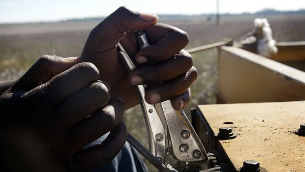 A close-up shot of two hands on a cotton module maker with farmland visible in the background.