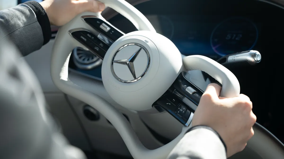 A driver's hands on the steering wheel of a Mercedes-Benz vehicle equipped with steer-by-wire technology.