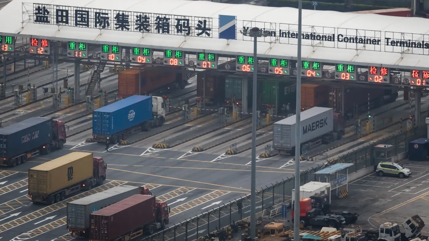 Trucks line up to enter a shipping terminal, as seen from overhead.