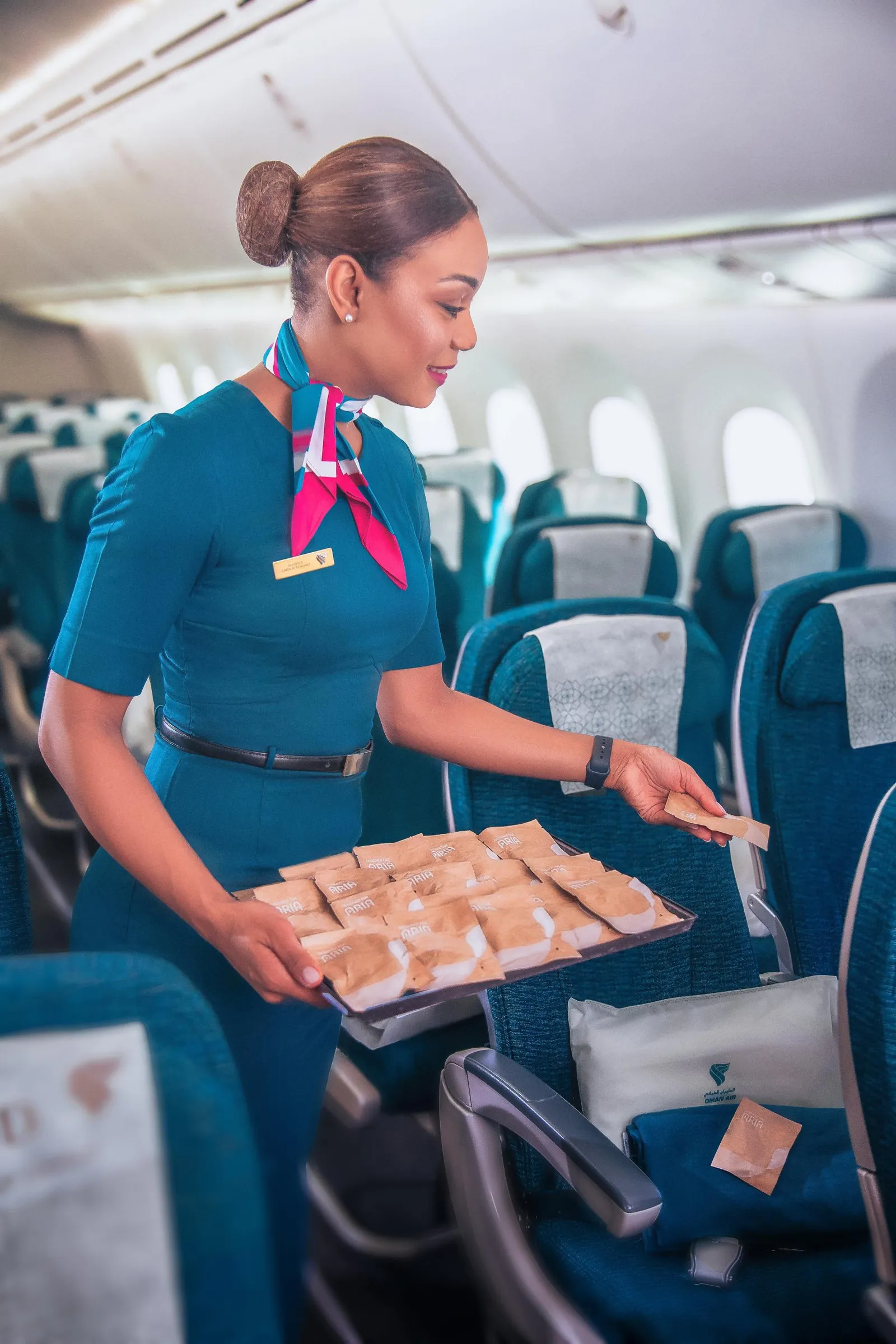 A flight attendant walks down the aisle of an airplane carrying a tray of earphones wrapped in paper envelopes.