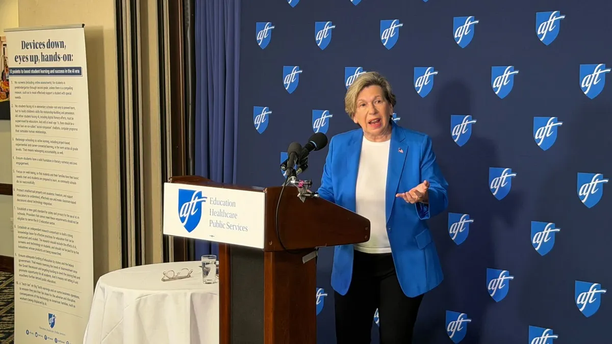 A person stands at a podium with behind a blue background with the American Federation of Teachers logo on it.