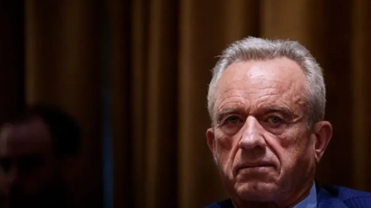 A person in a blue pinstripe suit looks straight ahead.