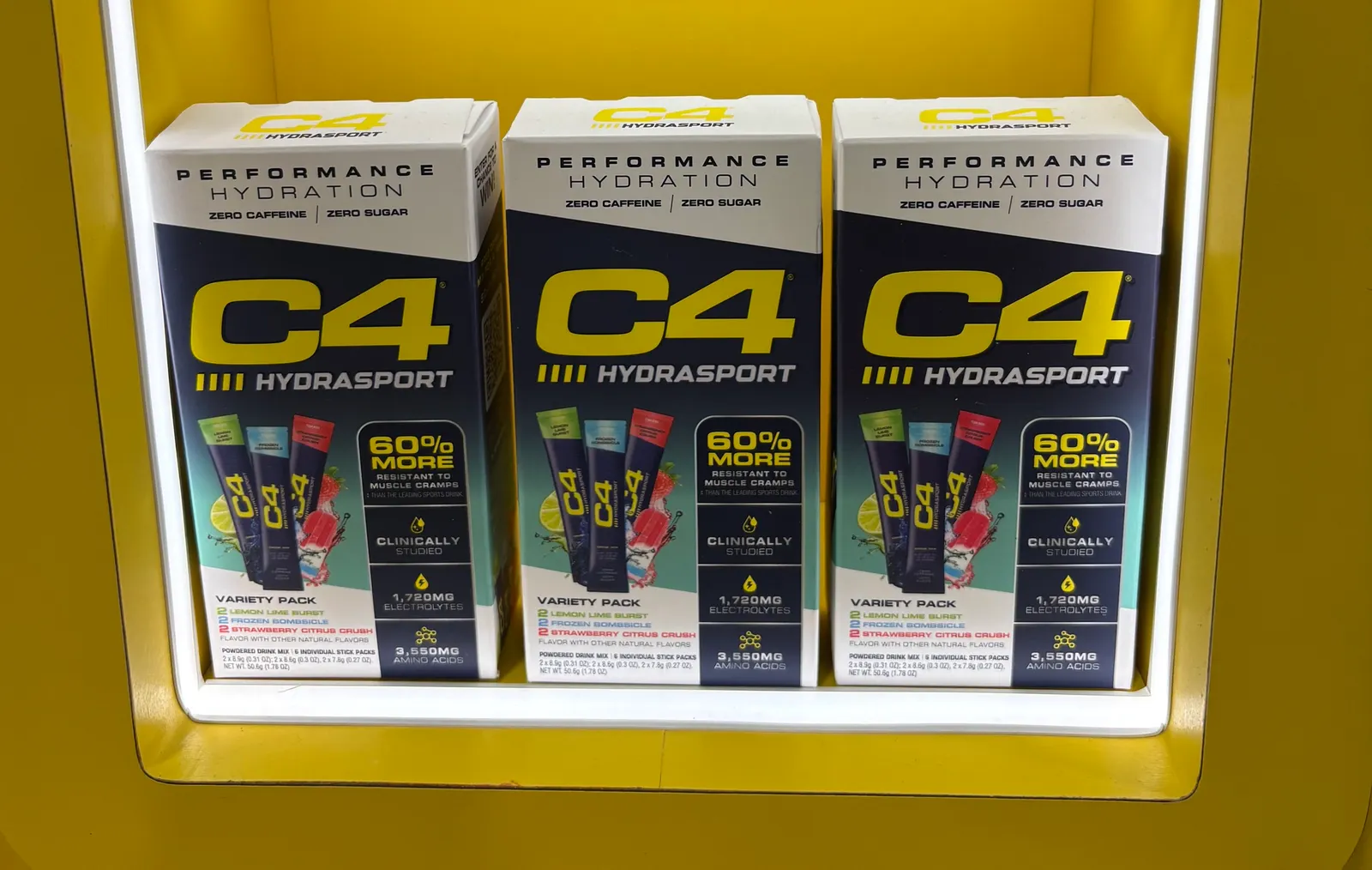 A photo of three boxes in a display set into a yellow wall. The boxes say C4 Hydrasport variety pack. 60% more resistant to muscle cramps.
