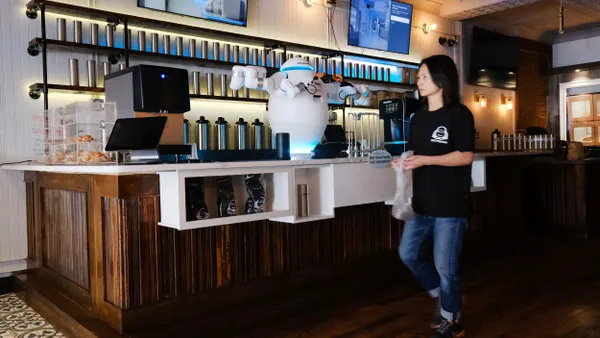 A person walks past a robot working at a cafe.