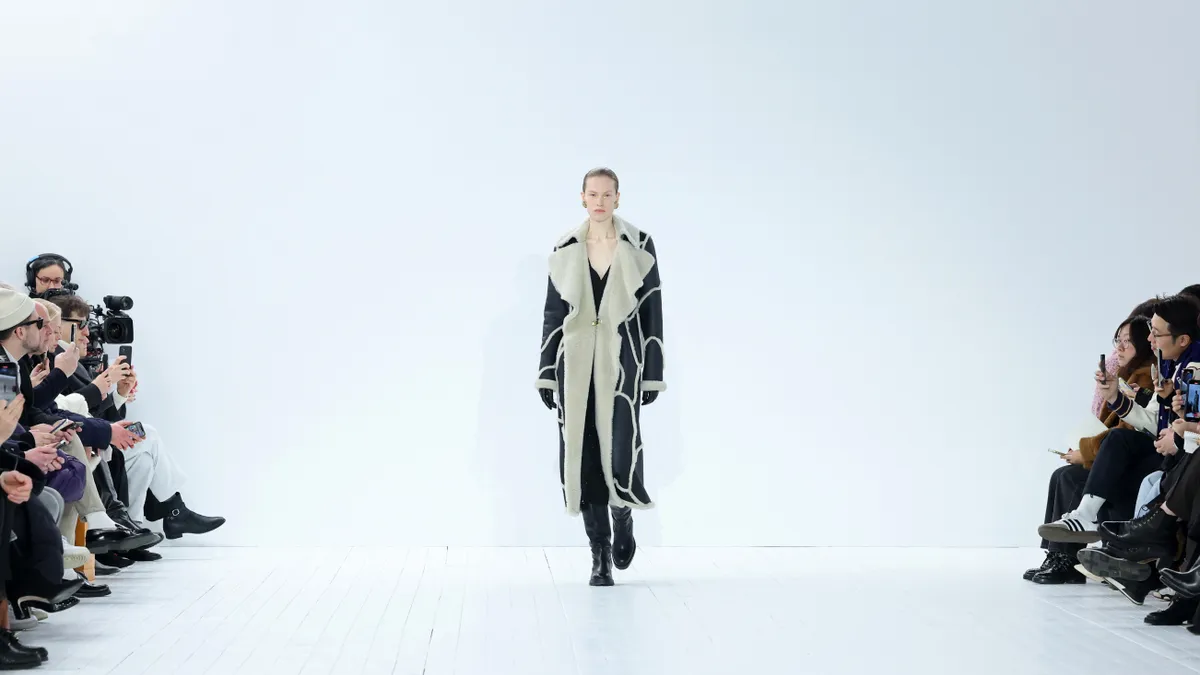 A model wears a black and tan coat and walks down a white runway for fashion brand Chloé.