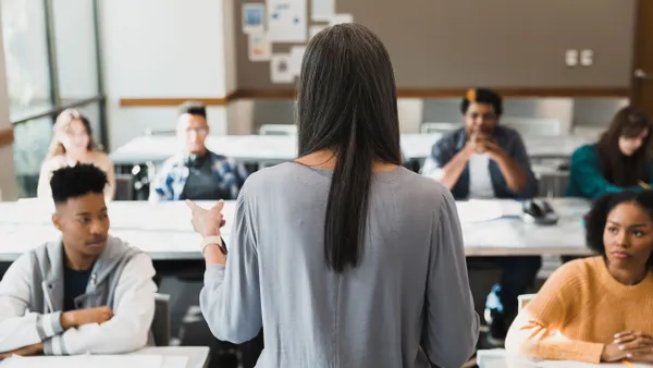 A teacher speaks to a classroom of students sitting at their desks.