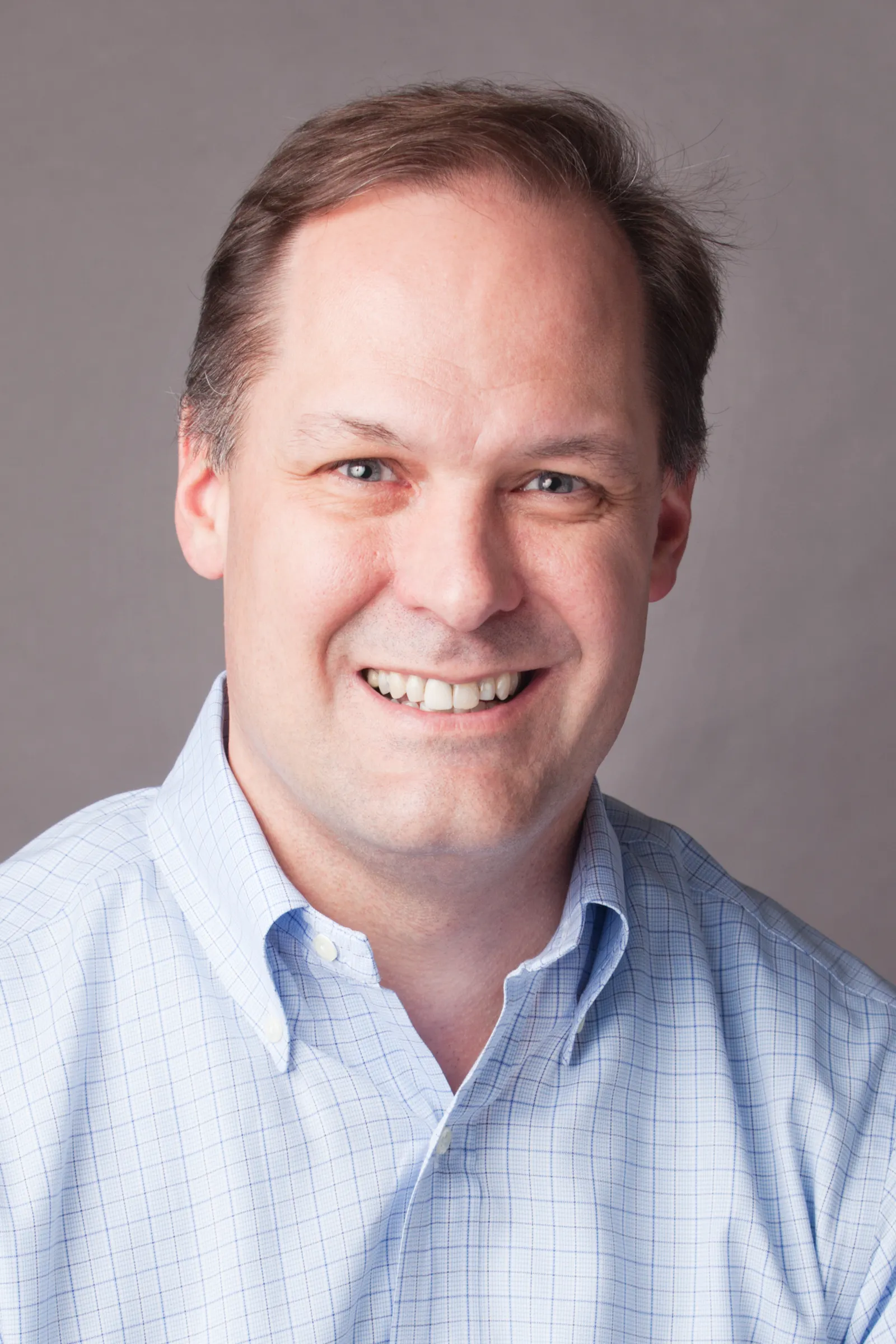 Michael Abbott poses for a photo wearing a button-down shirt in front of a gray background