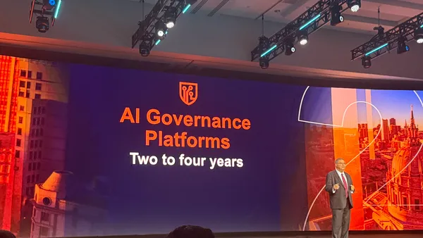 an analyst in business attire speaks on stage, with a screen in the background showing the text AI Governance Platforms.