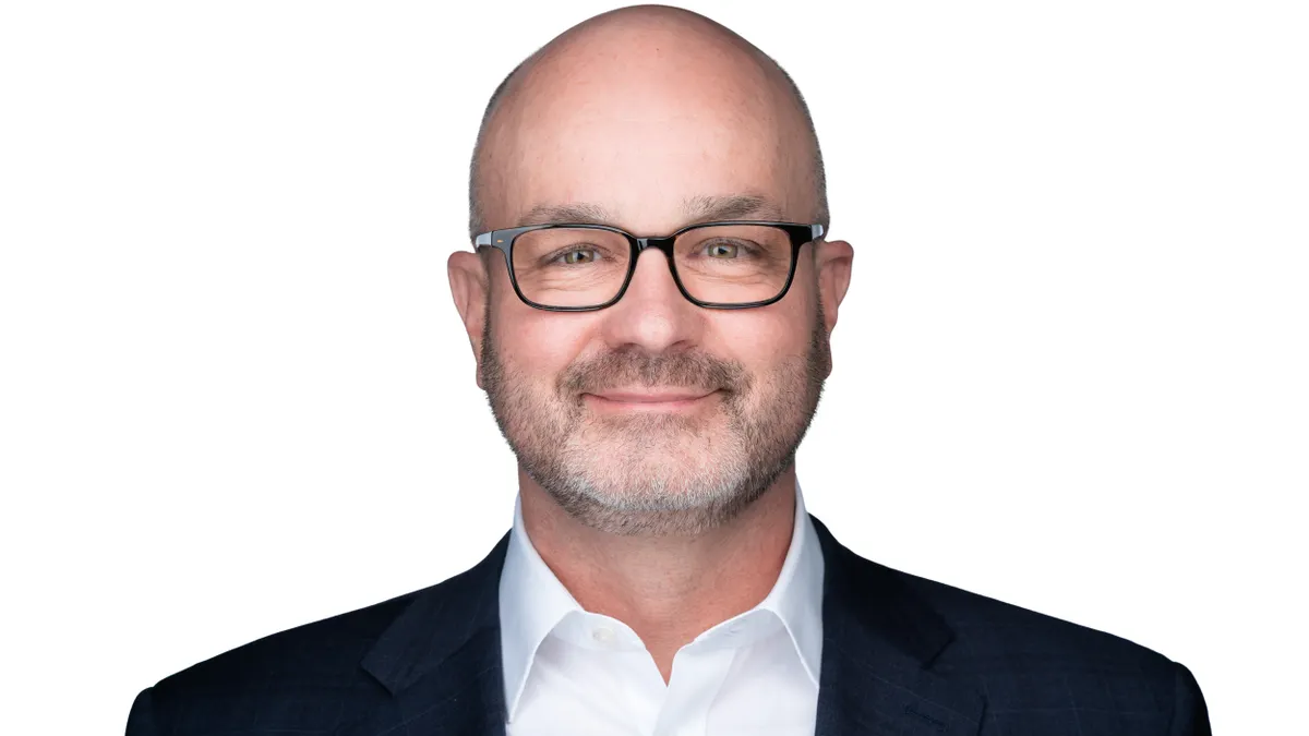 A portrait of a person smiling in a business suit and glasses.