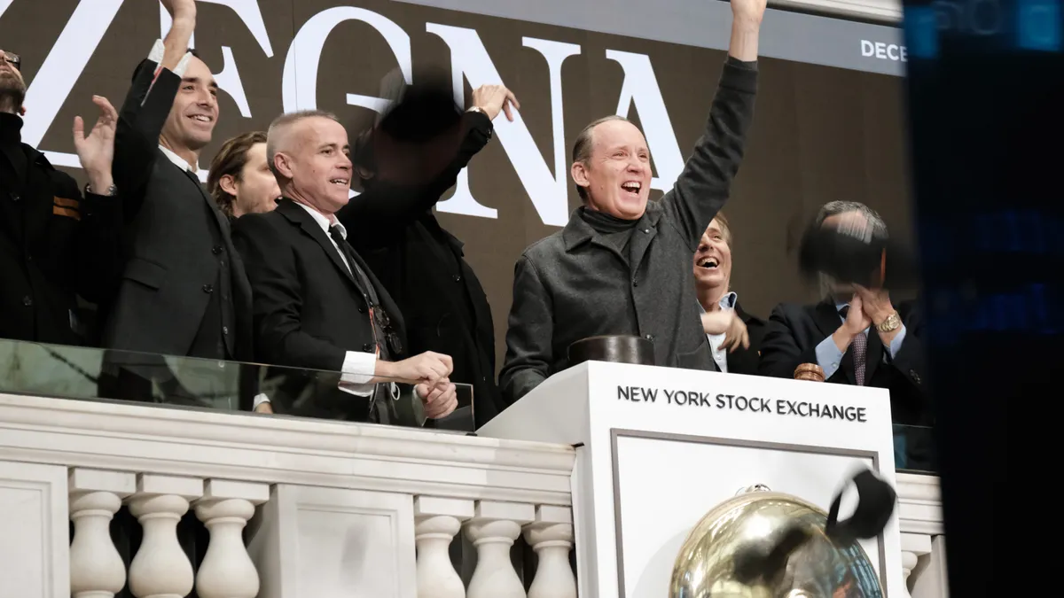 a group of men in black suits cheer in front of a backdrop that reads "Zegna" behind a podium that reads "New York Stock Exchange"