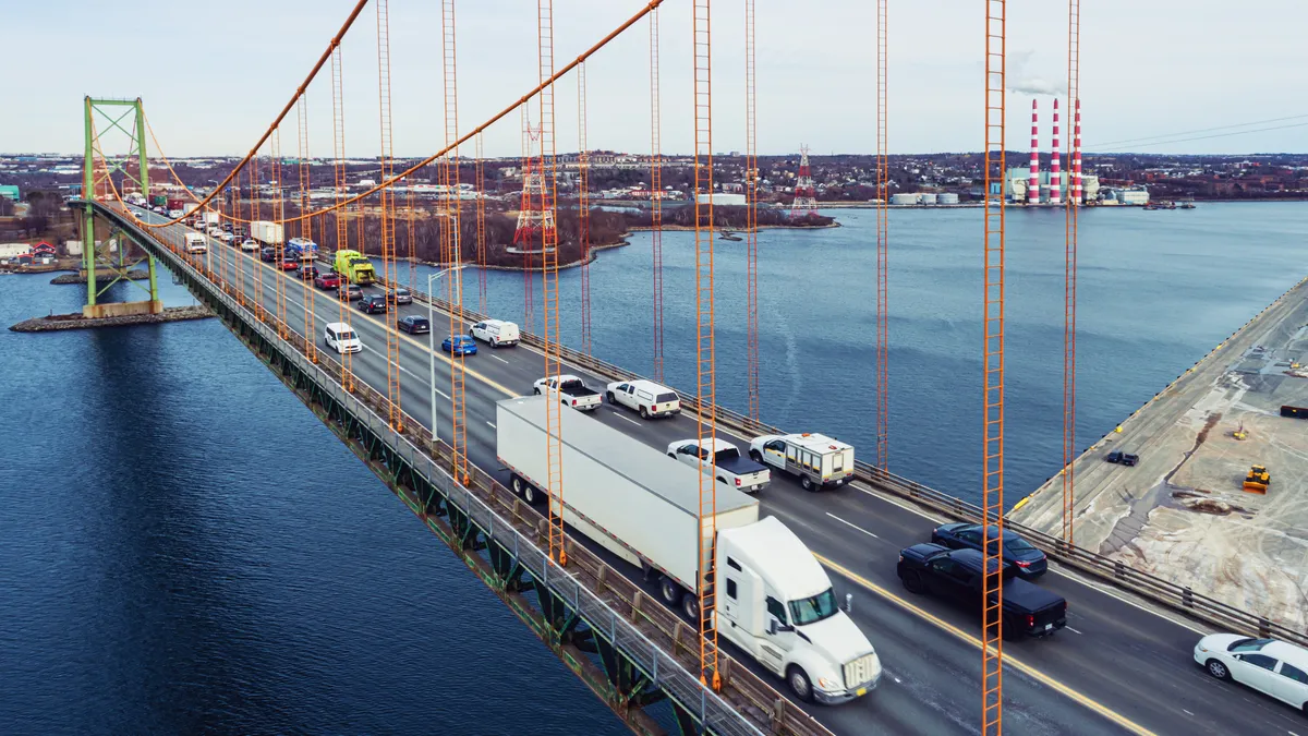 Aerial drone view of a tractor-trailer crossing a suspension bridge with heavy passenger traffic in the opposite lane.