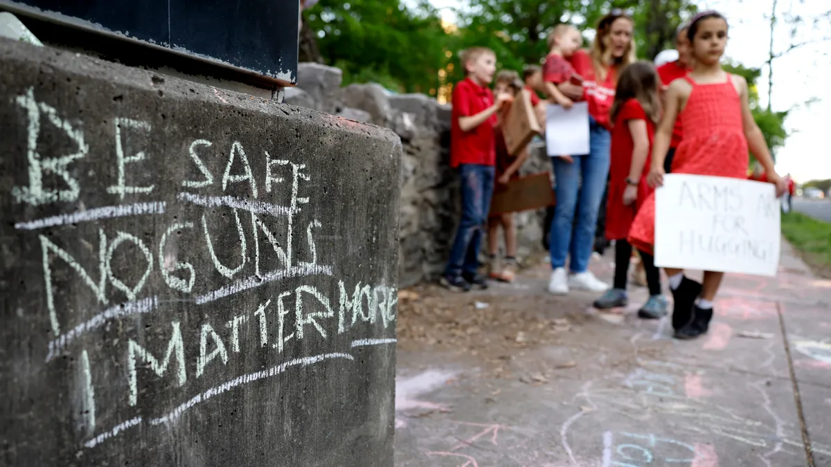 In the foreground is a chalkboard sign with anti-gun message. In the background are blurred images of children holding signs.