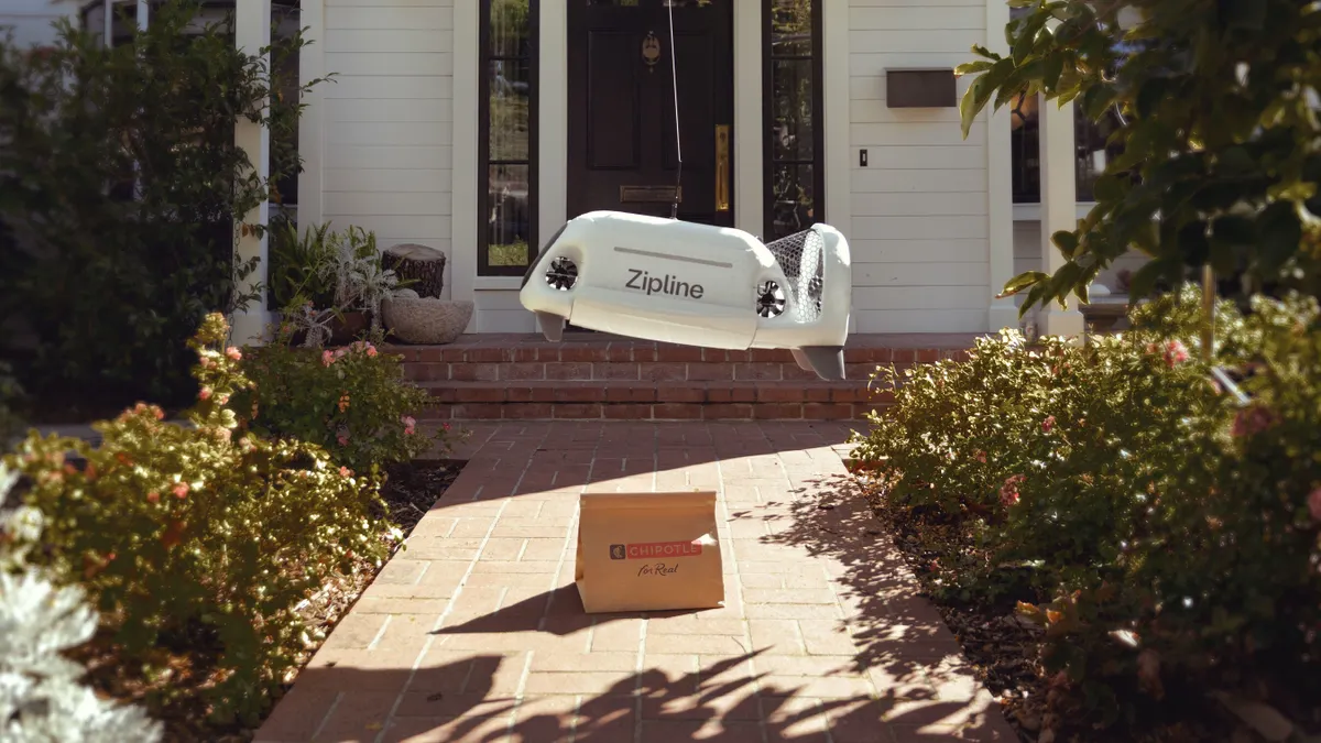 A photograph of a small drone-like device lowering a bag with a Chipotle logo on it to the ground.