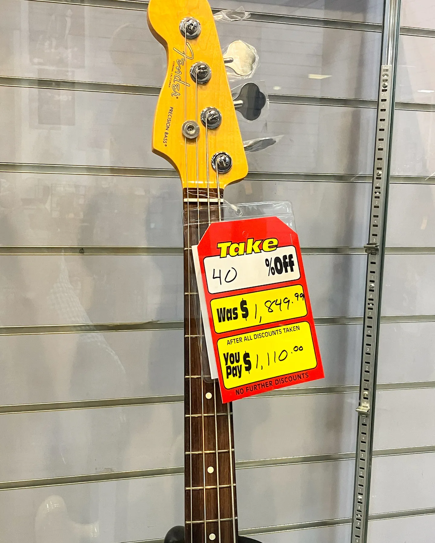 The headstock and neck of a Fender Precision electric bass guitar with a sale pricetag