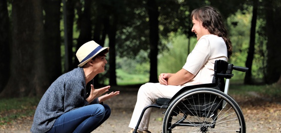 Person in a hat interacts with person in a wheelchair