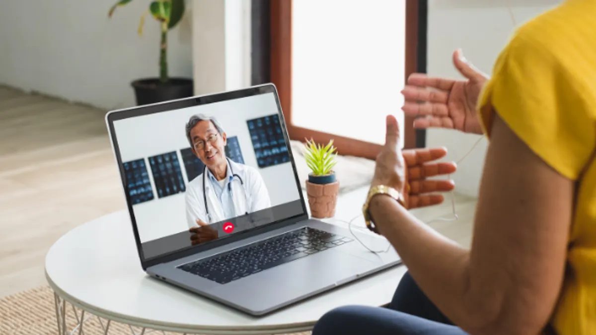 An adult with headphones in, having a telehealth appointment with a doctor on a laptop.