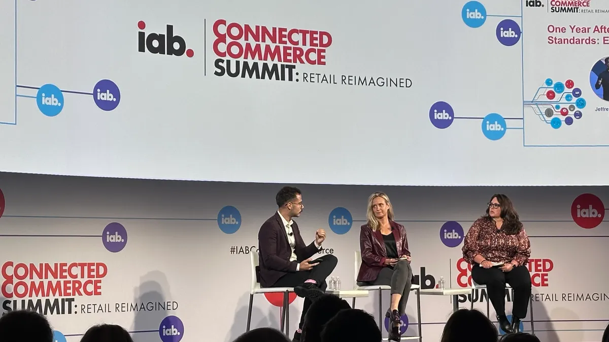 Three individuals on stage sitting on chairs talking to each other. Background is a white screen that reads "IAB Connected Commerce Summit."