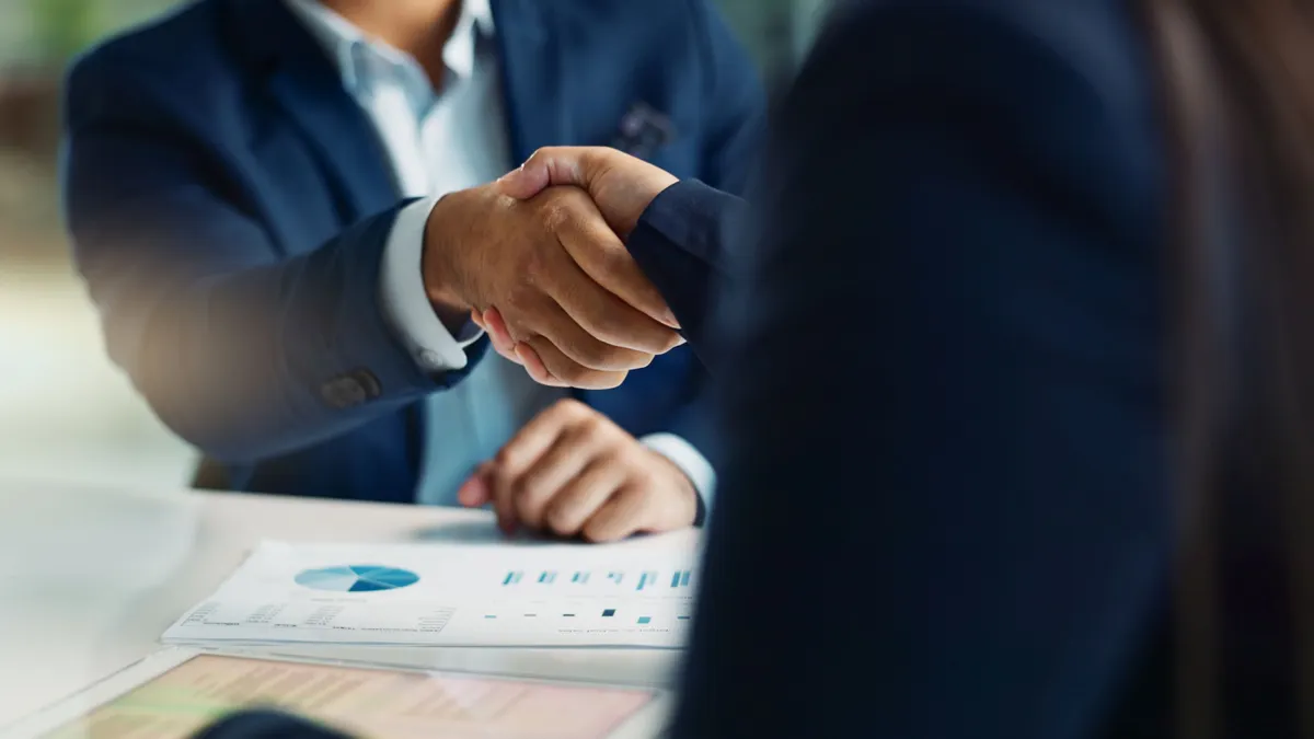 Two people in suits shake hands.