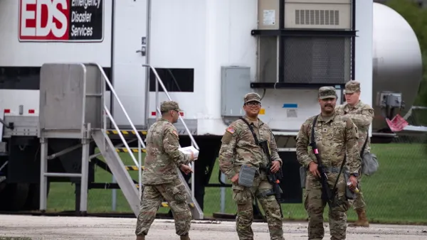 Three people in brown uniforms in front of a fence.