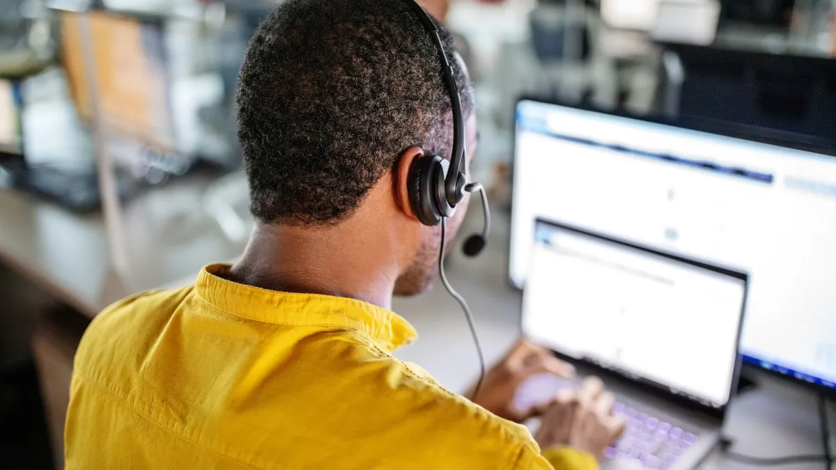 An employee wearing a headset sits at a workstation while using a computer.