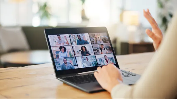 Photo of employee working on laptop at home and waving to colleagues in a video call