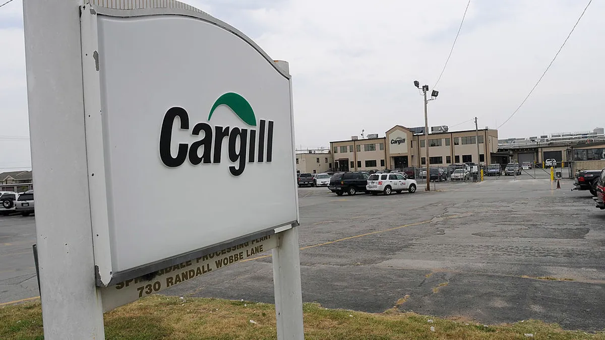 A sign reading "Cargill" is seen at the entrance of a parking lot to a factory building