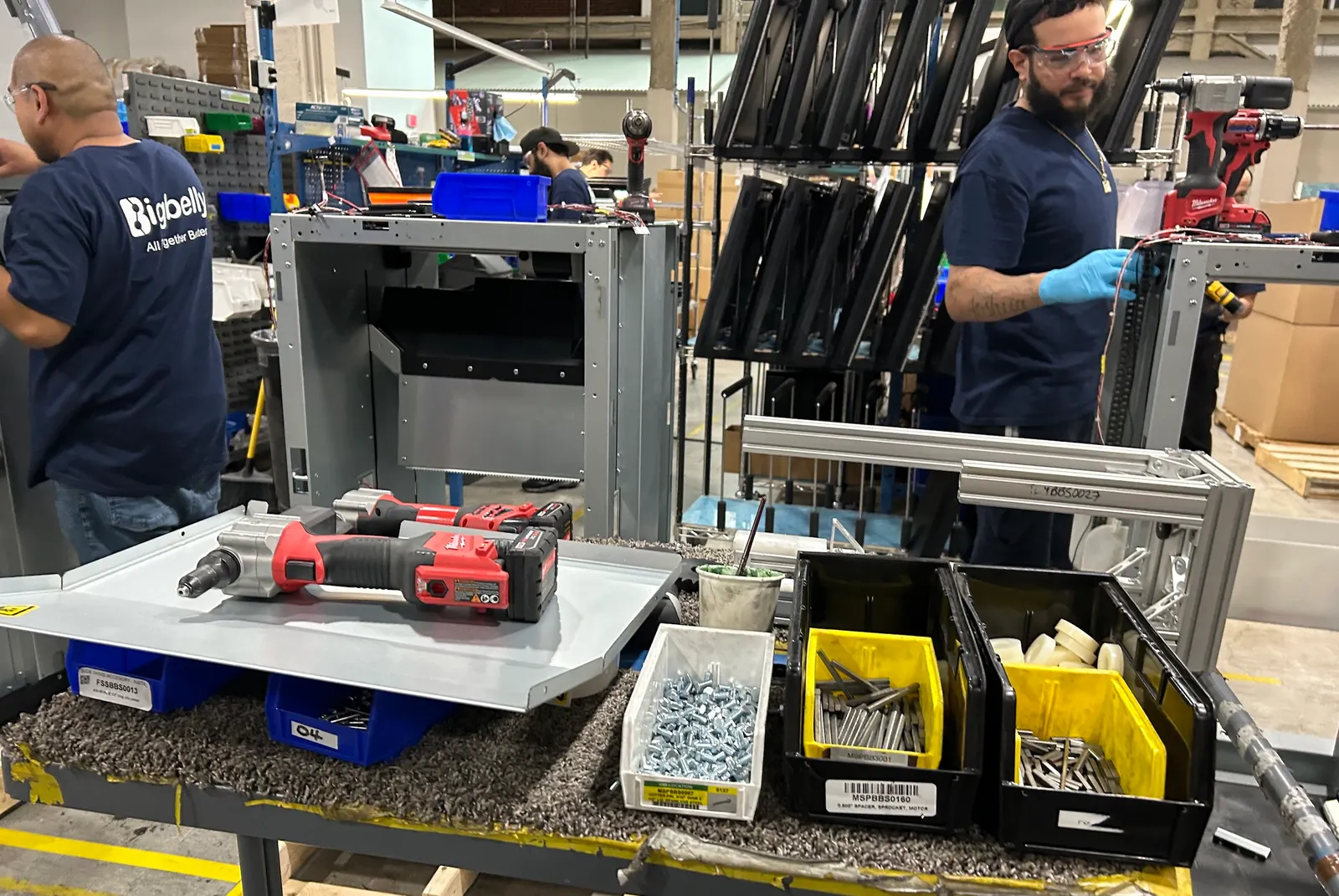 A bench of assembly tools, with workers wearing Bigbelly shirts in the background