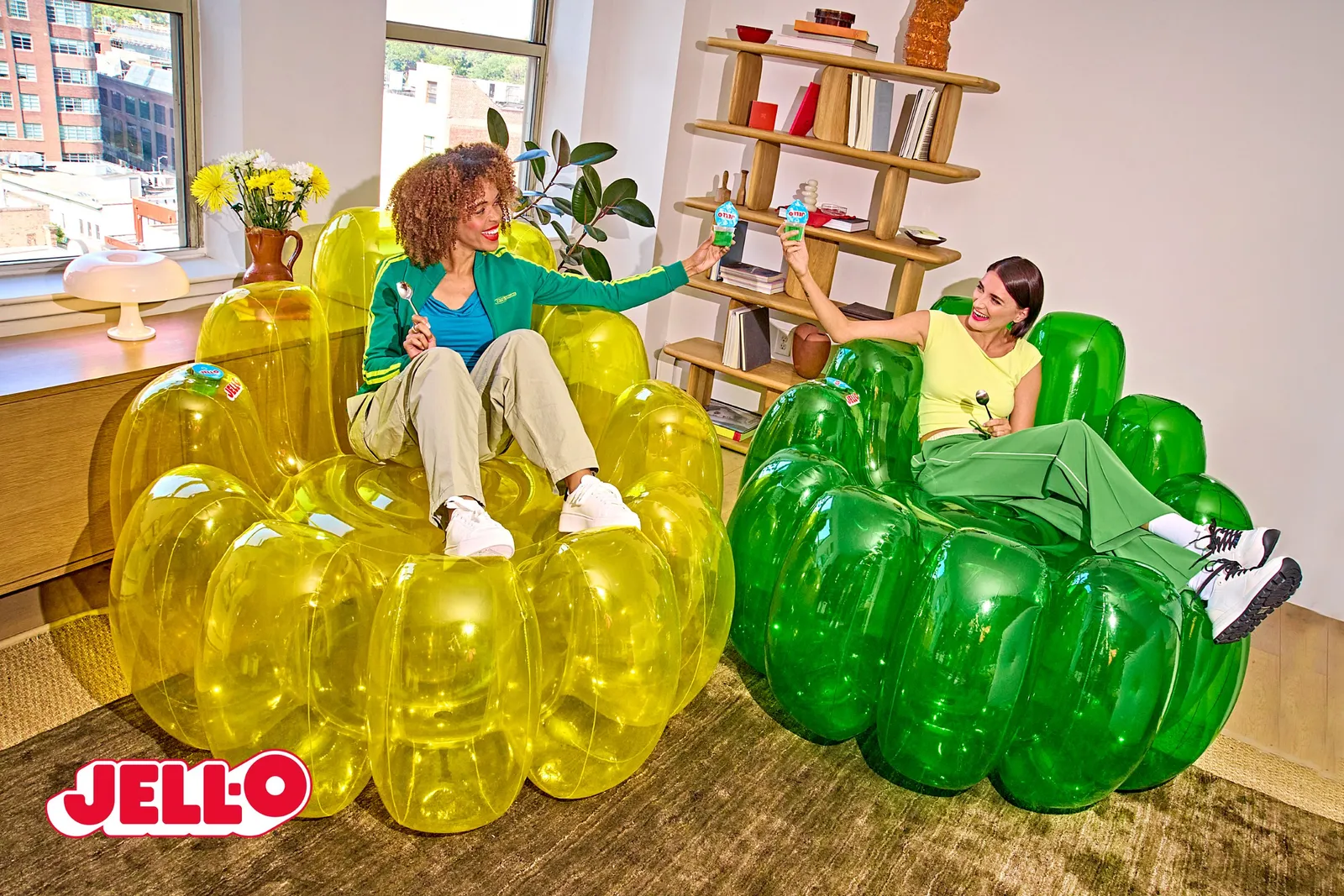 Two people sit on inflatable yellow and green chairs, cheersing with Jell-O cups.