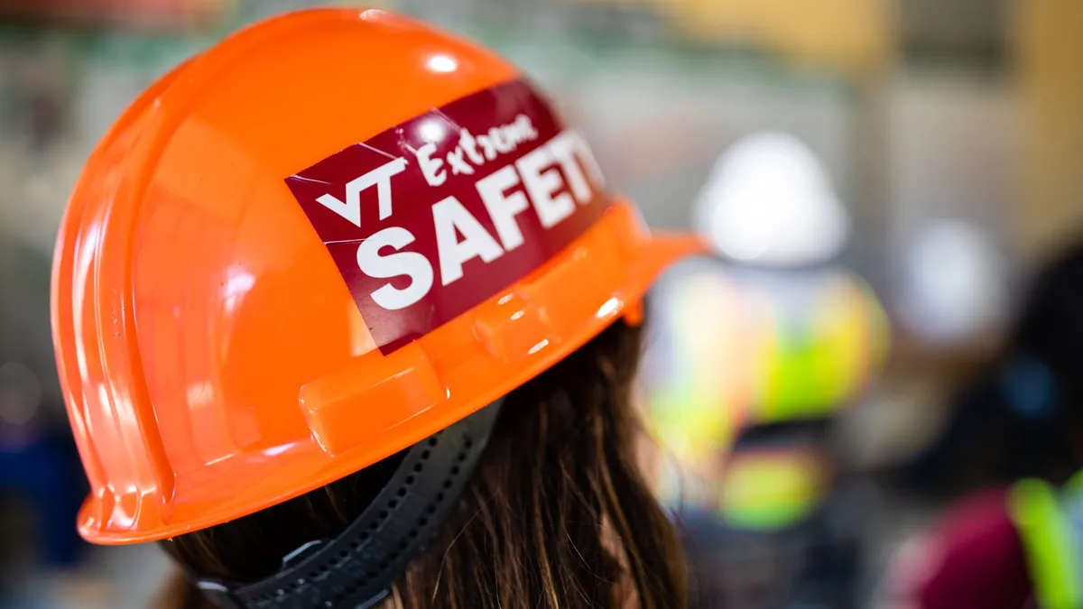 The back of a person's head wearing a bright orange Virginia Tech construction helmet.