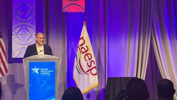 A person stands at a podium that says "National School Leaders Conference" on a stage.