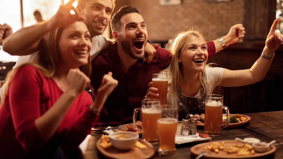 Happy friends cheering for their team while watching sports game on TV in a bar.